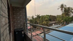 A balcony with a stone wall, a black object on the floor, and a view of palm trees and buildings in the background. - 1BHK Comfy Stay 5 (Pune)