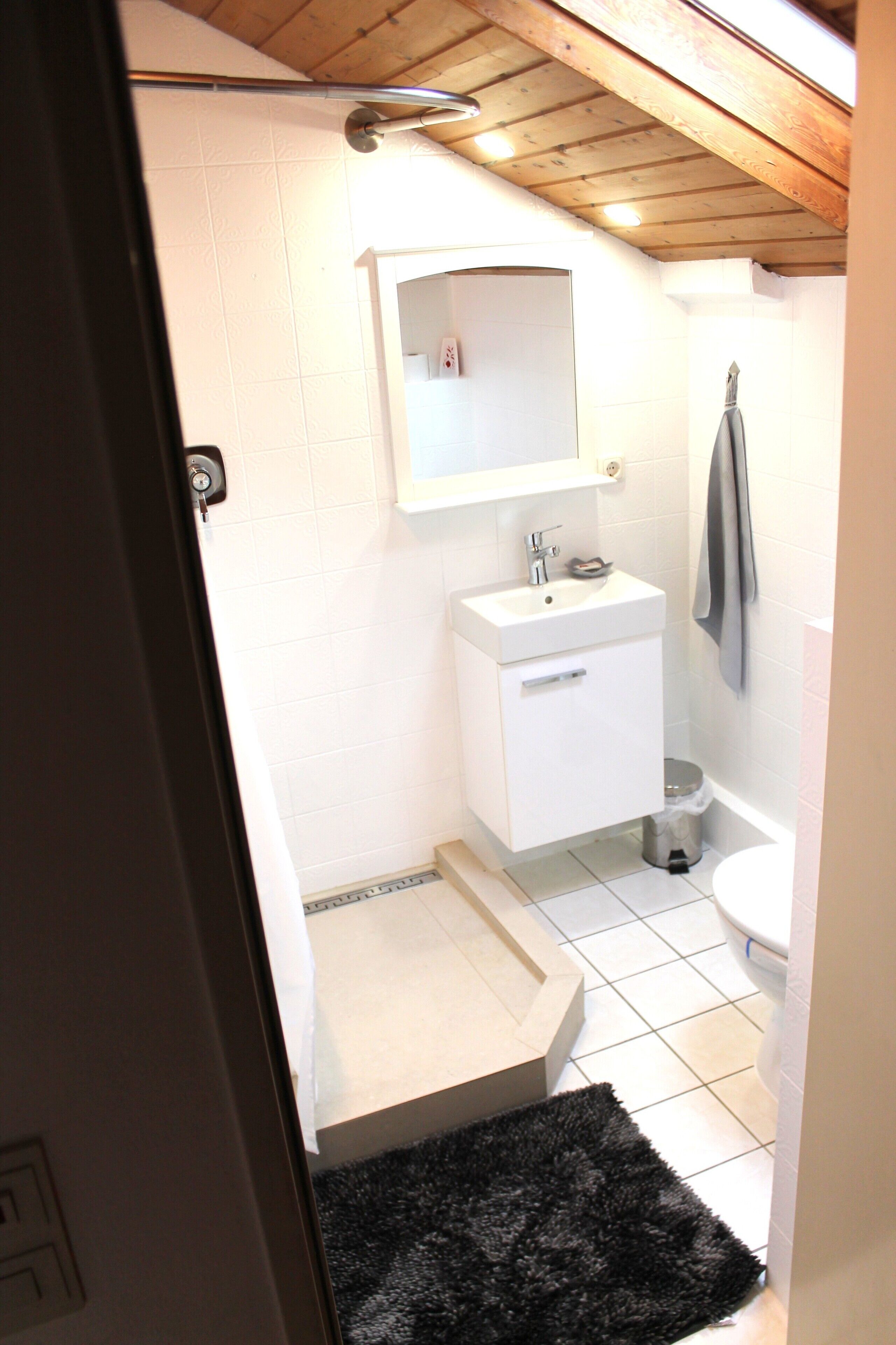 Et lille badeværelse med en hvid vask, et spejl, et håndklæde hængende på væggen og et toilet.