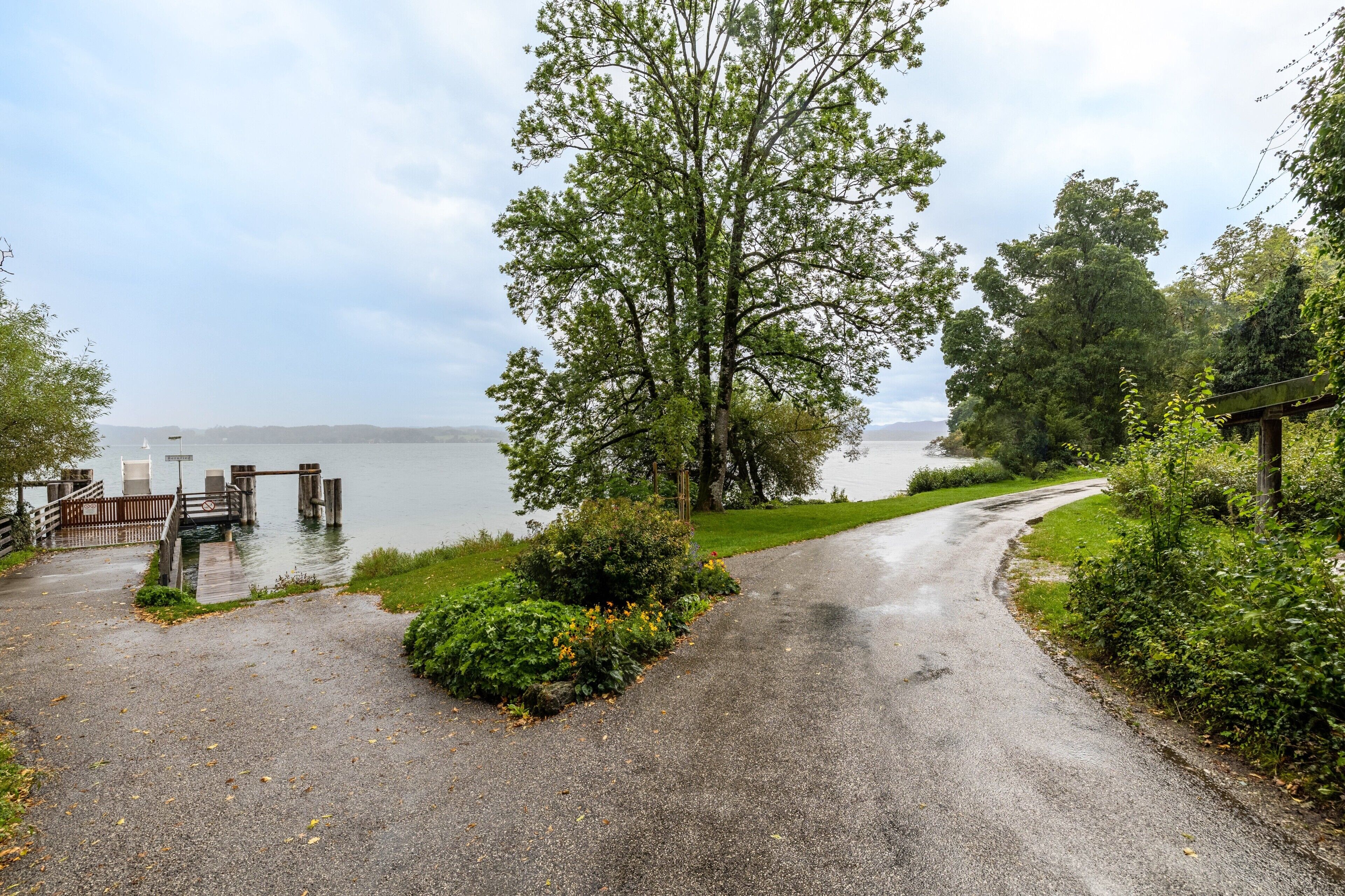 Un chemin pavé menant à un quai, bordé de verdure et donnant sur une étendue d’eau.
