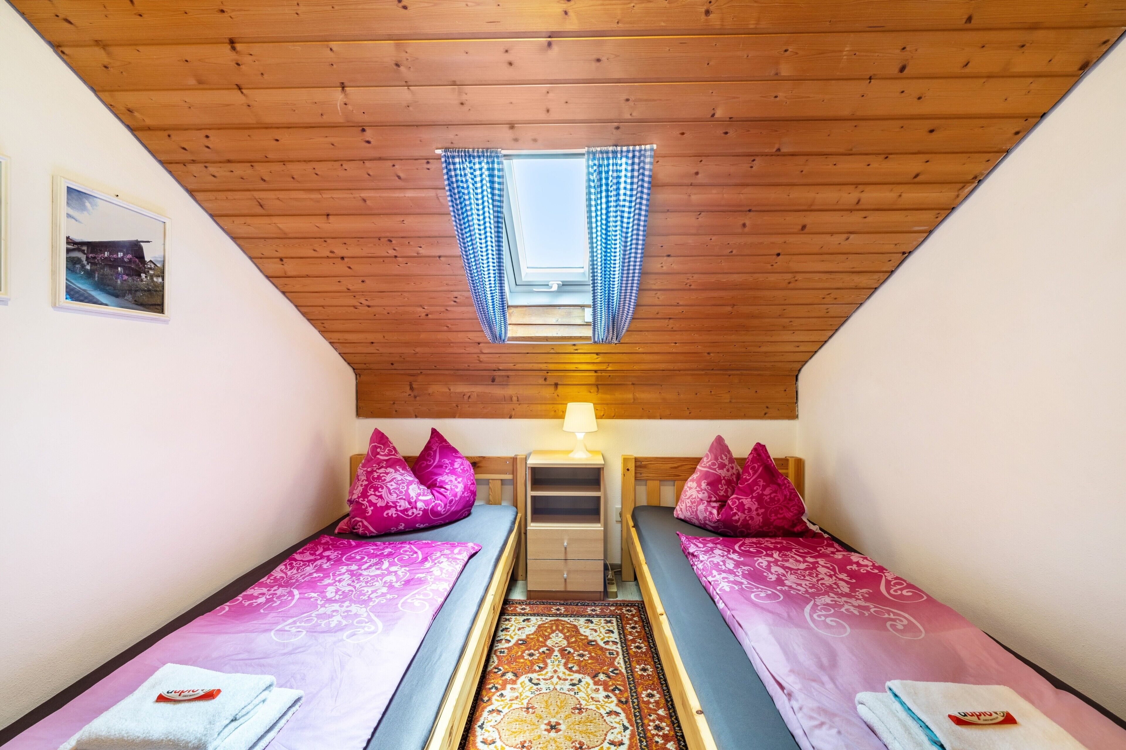 A room with two beds, a small table, a lamp, and a window with curtains.