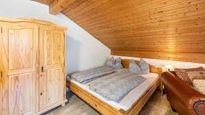 Eine Holzbalkendecke, ein Bett mit gemusterten Textilien, ein Holzschrank und ein Ledersofa.