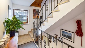 Eine Treppe mit Holzboden, ein Blumentopf, ein Fenster mit Vorhang und gerahmte Bilder an den Wänden.