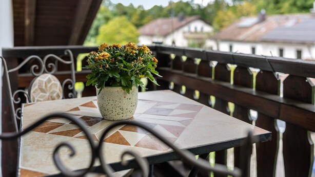 Ein Balkon mit Tisch, Blumentopf und Geländer.