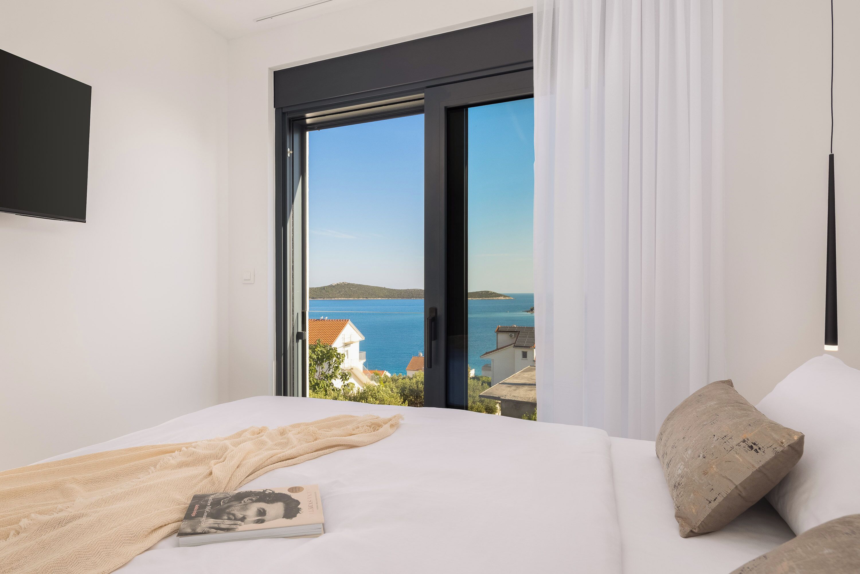 Une chambre à coucher avec un lit, une fenêtre donnant sur la mer et un téléviseur fixé au mur.