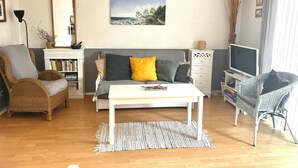A living room with a sofa, armchairs, a coffee table, a TV, and a bookshelf.