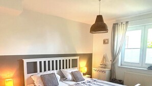 A bedroom with a bed, bedside tables, a lamp, a window with curtains, and a hanging light fixture.