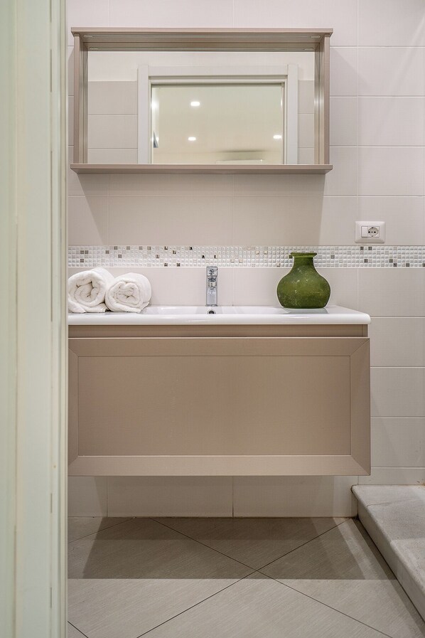 Un baño con un lavamanos blanco, un florero verde y un perchero.