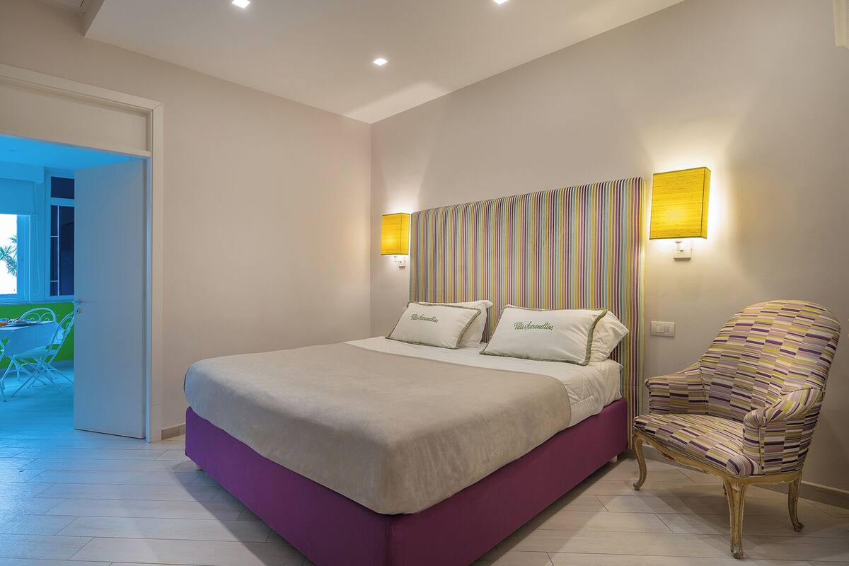 Un dormitorio con una cama, dos lámparas de noche, una silla y vistas a un balcón.