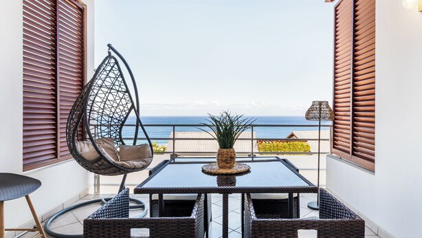 A balcony with a hanging chair, a table with a potted plant, and a view of the sea.