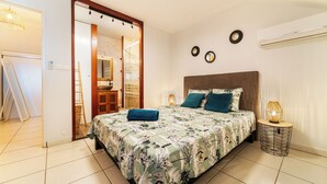 A bedroom with a bed, a bedside lamp, a mirror, and a door leading to another room.