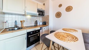 A modern kitchen with white cabinets, a microwave, a toaster, and a sink. There are woven placemats on the table and a small oven.
