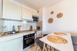 Eine moderne Küche mit weißen Schränken, einer Mikrowelle, einem Toaster und einem Spülbecken. Auf dem Tisch liegen gewebte Tischsets und ein kleiner Backofen.