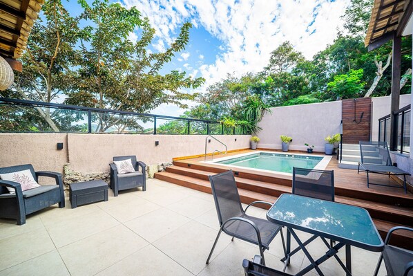 An outdoor patio with a pool, wicker furniture, and a view of trees and sky.