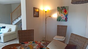Ein Wohnzimmer mit Sofa, Korbstühlen, einem Esstisch mit Laptop, einer Stehlampe und Kunstwerken an der Wand.