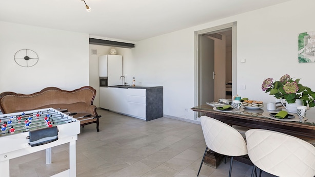 Un soggiorno moderno con un tavolo da calcio, un divano, una zona pranzo con sedie, un'isola cucina e una lampada a sospensione.