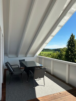 Un balcón con mesa y sillas, vista a un paisaje verde y cielo azul despejado.