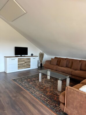 Una sala de estar moderna con una televisión de pantalla plana, un sofá marrón, una mesa de centro de vidrio y una alfombra estampada.