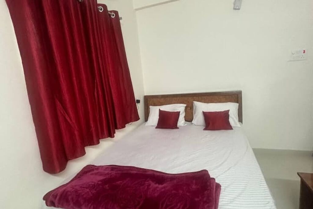 A single bed with a wooden headboard, white bedding, and red curtains.