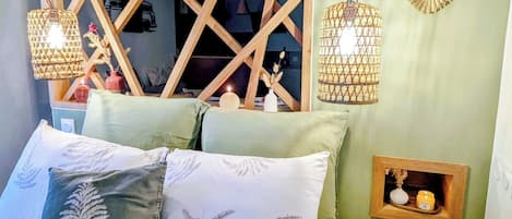A bedroom with a bed, pillows, a wooden headboard, and two hanging lamps.