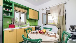 A compact kitchen with green cabinets, a dining table with chairs, and a window with curtains. - Villa Klio (Pitsidia Heraklion Crete)