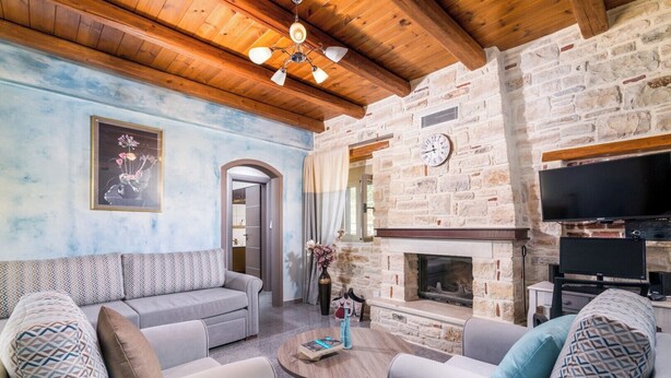 A cozy living room with a stone fireplace, a sofa set, and a television. - Villa Klio (Pitsidia Heraklion Crete)