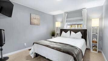 Une chambre à coucher avec un lit, une télévision, une lampe et une fenêtre avec des rideaux.