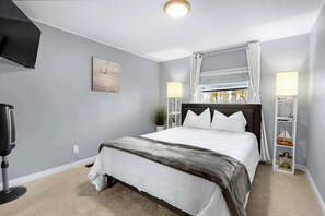 A bedroom with a bed, a TV, a lamp, and a window with curtains. - Amazing Lakefront Escape - A Stunner For Sleeps 14 (New Braunfels)