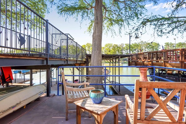A wooden deck with a table and chairs, overlooking a body of water with boats and a dock. - Amazing Lakefront Escape - A Stunner For Sleeps 14 (New Braunfels)