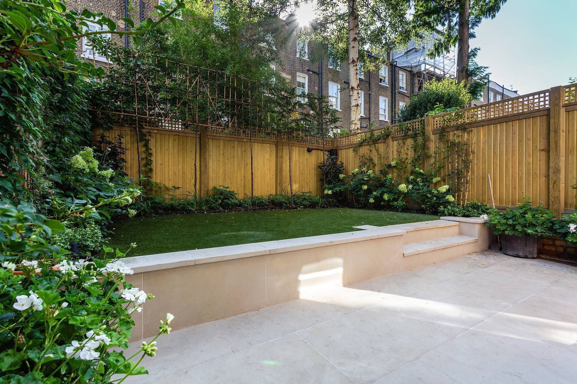 A backyard with a wooden fence, a grassy lawn, and a concrete patio area.