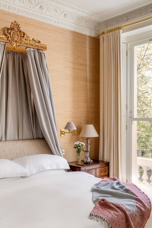 A bedroom with a canopy bed, a nightstand with a lamp, and a view of the outdoors.