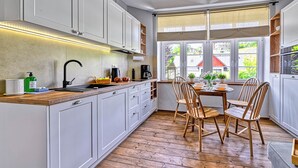 A modern kitchen with white cabinets, a wooden countertop, and a dining area with wooden chairs. - Apartamenty Sun & Snow Strażacka (Karpacz)