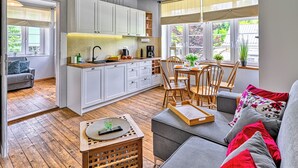 A modern kitchen with white cabinets, a dining area with wooden chairs, and a sofa with red cushions. - Apartamenty Sun & Snow Strażacka (Karpacz)