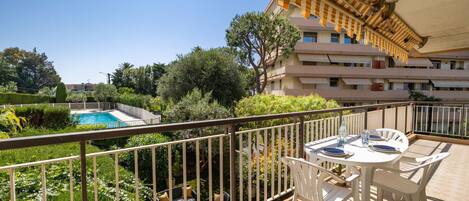 A balcony with a pool, white furniture, and a view of a building with balconies.