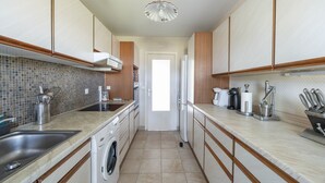 Een moderne keuken met een spoelbak, fornuis en koelkast. Een deur leidt naar een andere kamer.