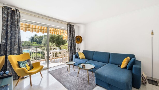 Een moderne woonkamer met een blauwe bank, een gele fauteuil en twee glazen salontafels.