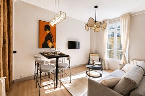 Una sala de estar moderna con un sofá, comedor con sillas, un televisor montado en la pared y un ventanal con cortinas.