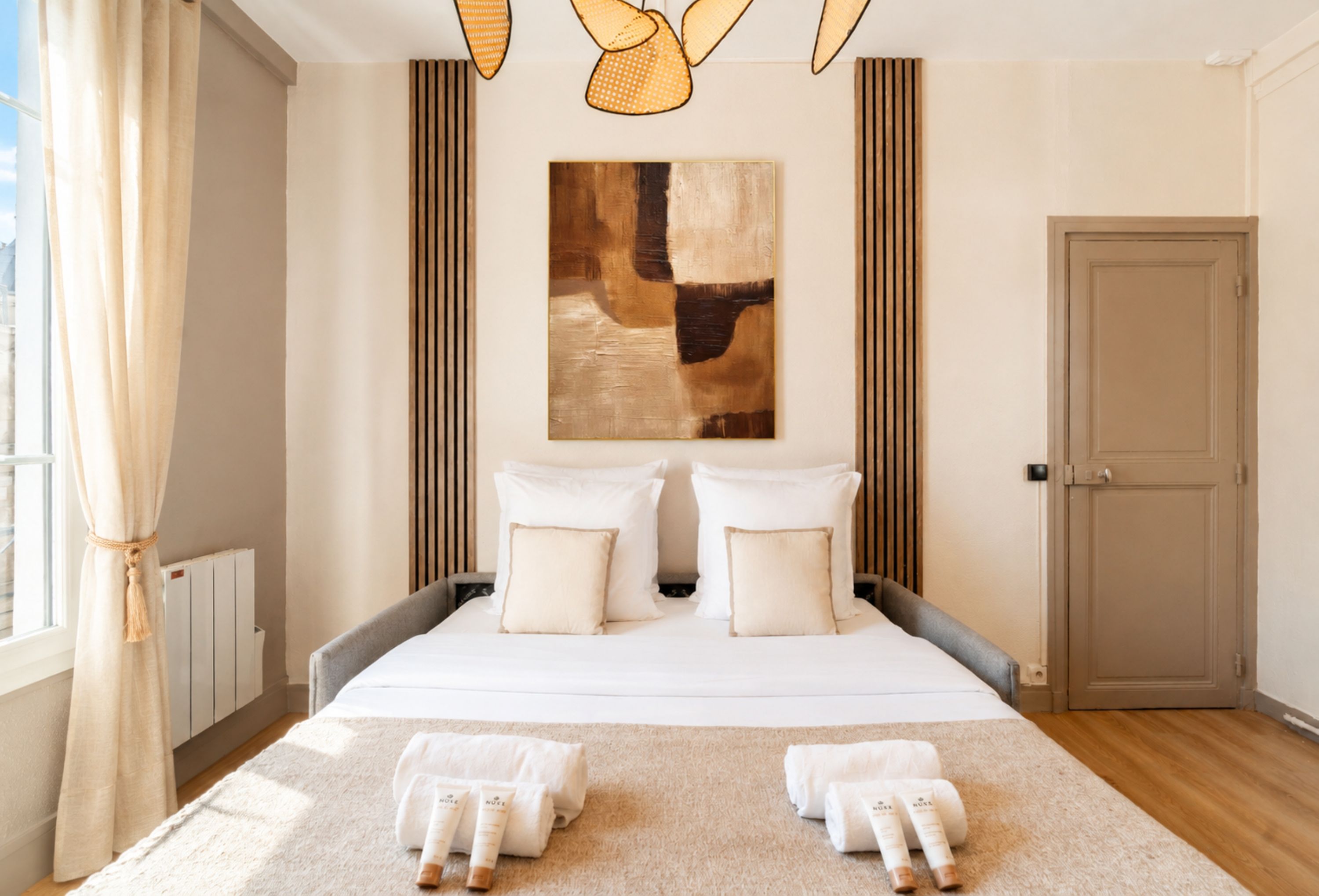 Une chambre d’hôtel avec un grand lit, deux oreillers, une tête de lit, une porte, un radiateur et une fenêtre avec des rideaux.