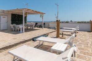 Een terras op het dak met witte lounge fauteuils, een kleine tafel en een overdekte zithoek met stoelen en een tafel.