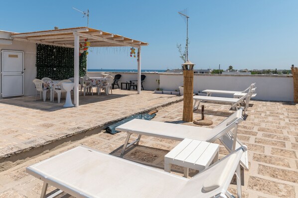 A rooftop terrace with white lounge chairs, a small table, and a covered seating area with chairs and a table.