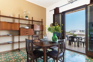 Een eetgedeelte met een houten tafel en stoelen, een vaas met bloemen en uitzicht op het balkon.