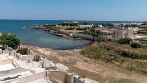 A coastal residential area with houses, a rocky shoreline, and a clear view of the sea.