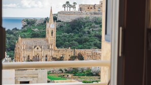 A balcony with a view of a historic church and surrounding greenery. - Luxurious Gozo penthouse with sea view & pool (Għajnsielem)