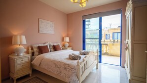 A bedroom with a bed, nightstands, a chandelier, a large window, and a view of the outside. - Luxurious Gozo penthouse with sea view & pool (Għajnsielem)
