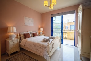 A bedroom with a bed, nightstands, a chandelier, a large window, and a view of the outside.