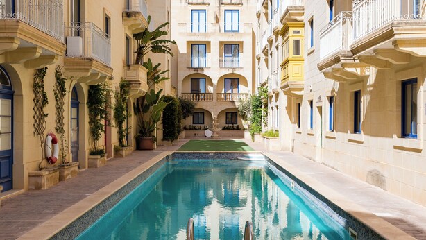 A pool area with a clear view of the pool, surrounded by buildings with balconies and windows. - Luxurious Gozo penthouse with sea view & pool (Għajnsielem)