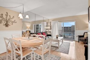 A modern living room with a dining area, large windows, and a balcony. - Oceanfront Creston House Condo (Unit 5C) (St. Augustine)