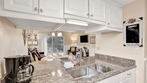 A modern kitchen with granite countertops, stainless steel appliances, and white cabinetry. - Oceanfront Creston House Condo (Unit 5C) (St. Augustine)