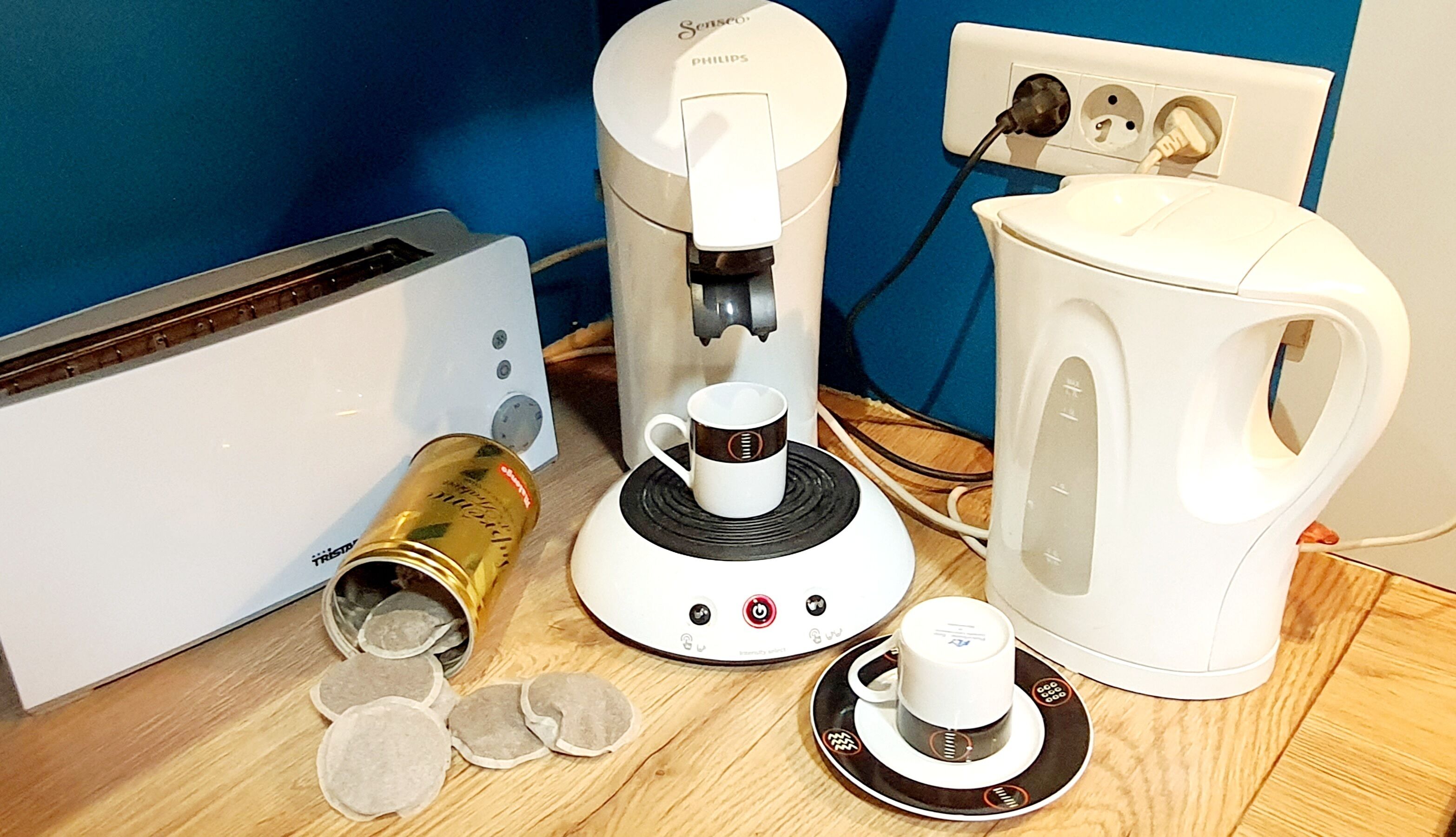 A coffee maker, a kettle, and a cup on a wooden table.