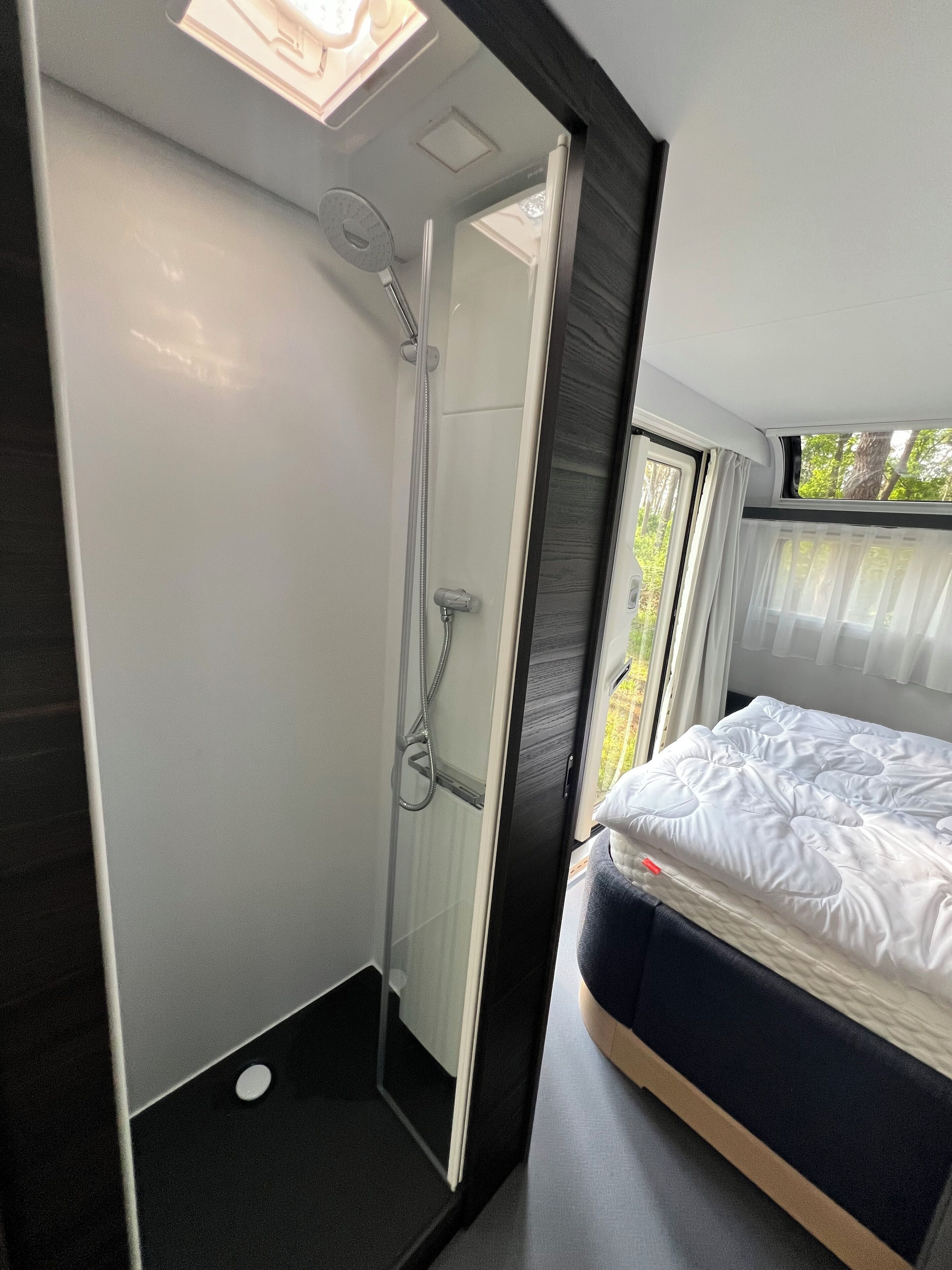 A modern bathroom with a shower, a toilet, and a bed with a mattress and pillows.