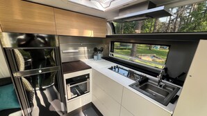 A compact kitchen with a built-in oven, a sink, and a window overlooking a garden. - Luxury caravan 5 with whirlpool directly on the Achterwasser -holiday homes island Usedom (Lütow)